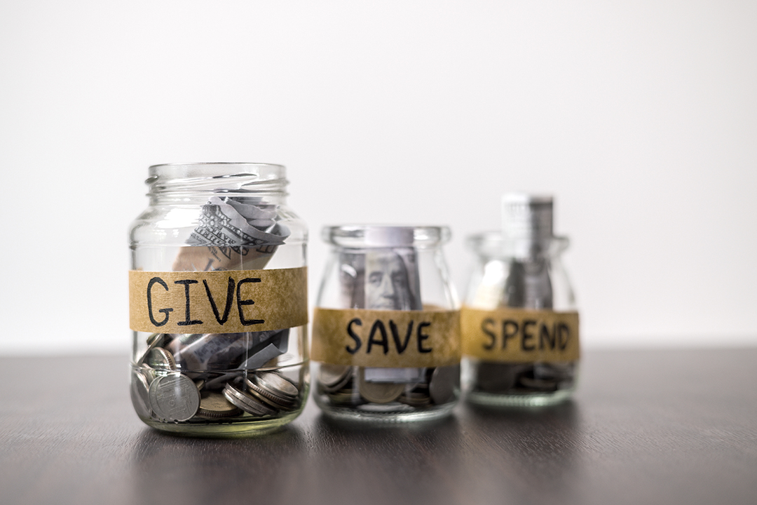 Three jars sit on a table each with labels saying Give Save Spend.