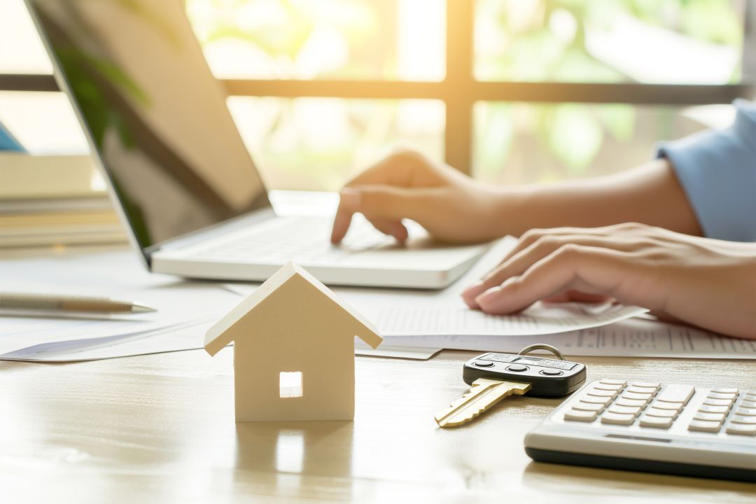 Close up of someone working on a laptop with a toy house and keys