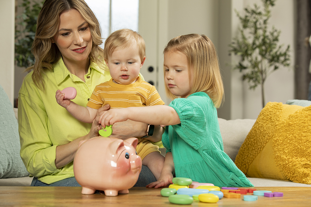 A mother with two small kids enjoys saving money using a piggy bank.