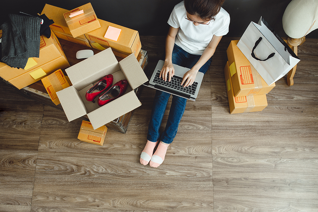 A person typing on a laptop surrounding by boxes.