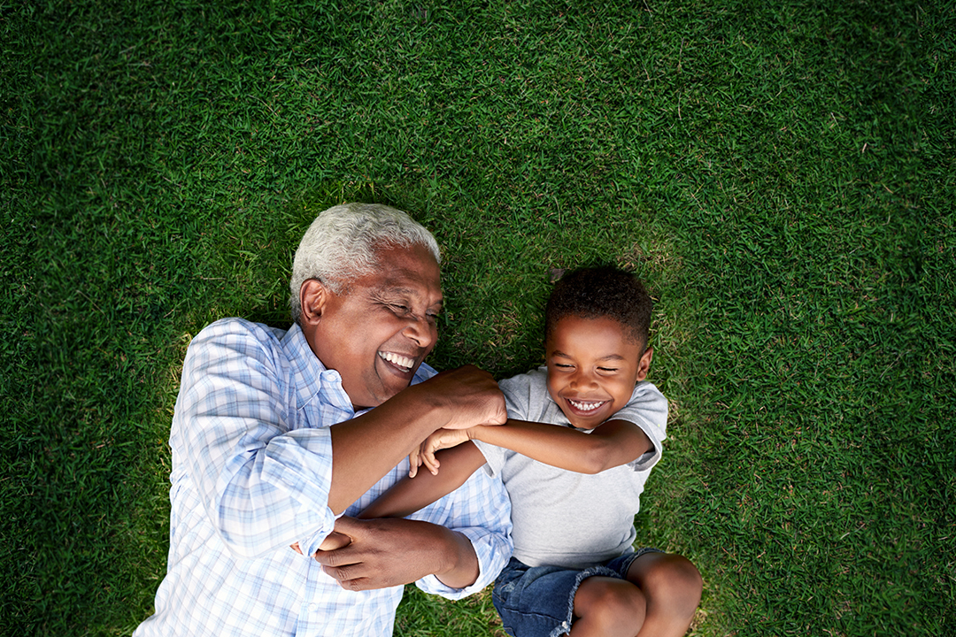 Grandfather and grandson playing and laughing in grass.
