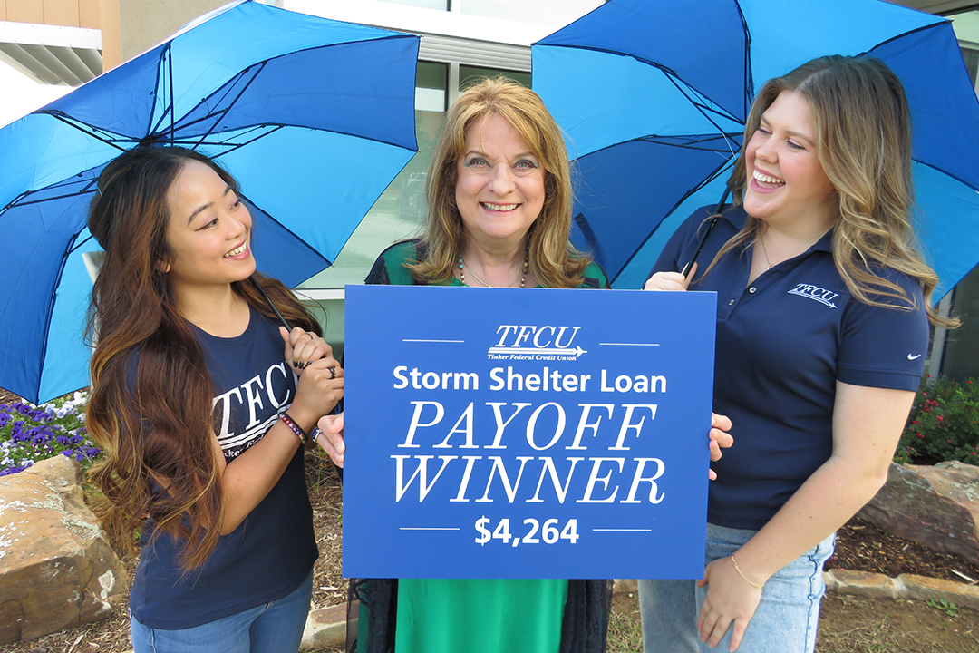 Two TFCU employees looking at a TFCU member while she is holding a sign that says storm shelter loan payoff winner