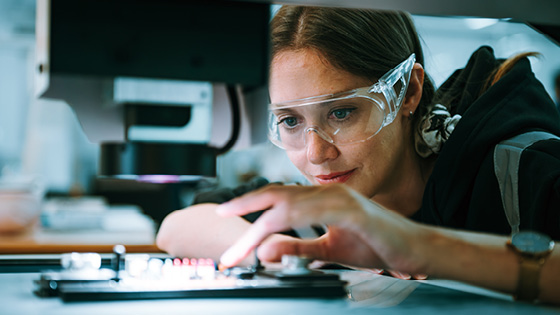 Close up of a woman with safety glasses looking and working with a mechanical equipment.