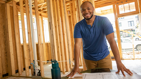 A smiling man who is a contractor is in a construction home with blueprints.