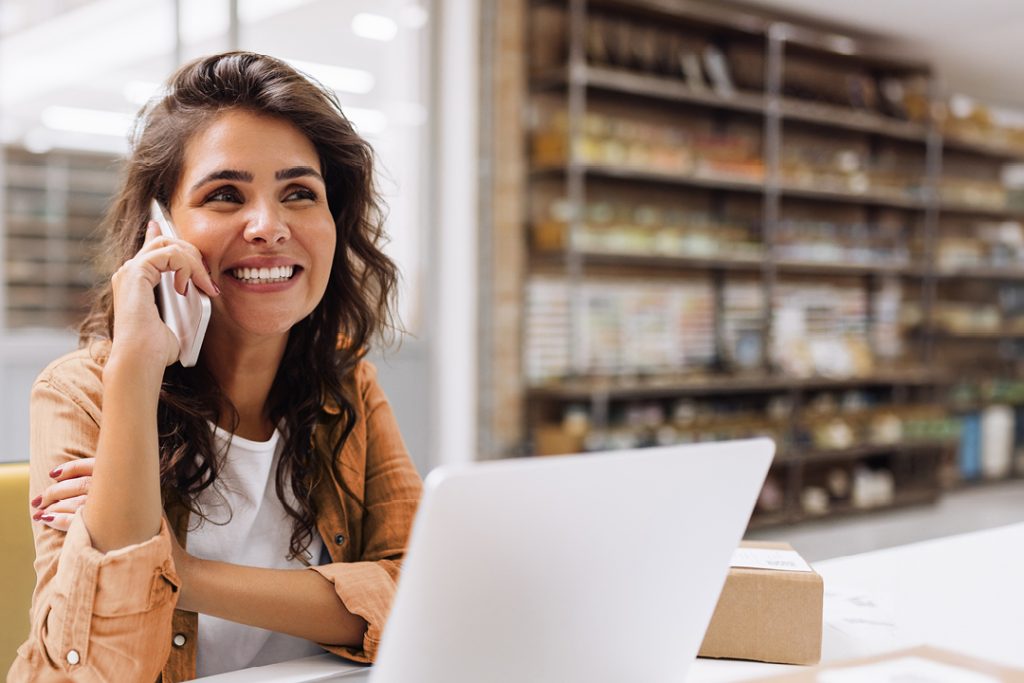 A woman talking on her phone while on a laptop.