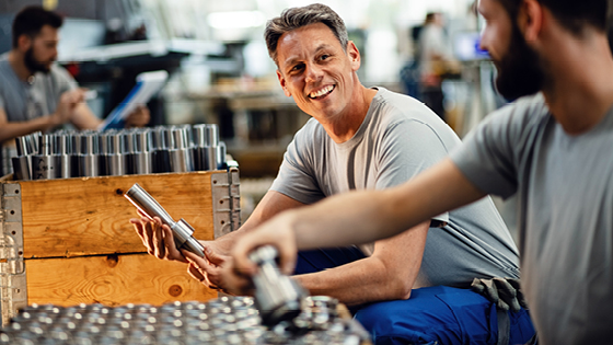 An older man looking at another man while holding an industrial metal piece