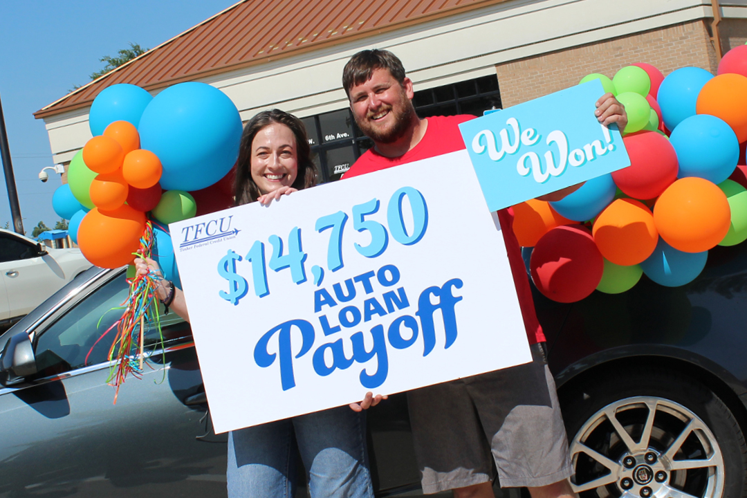 A man and woman standing in front of a car and colorful balloons and holding a sign that says $14,750 auto loan payoff