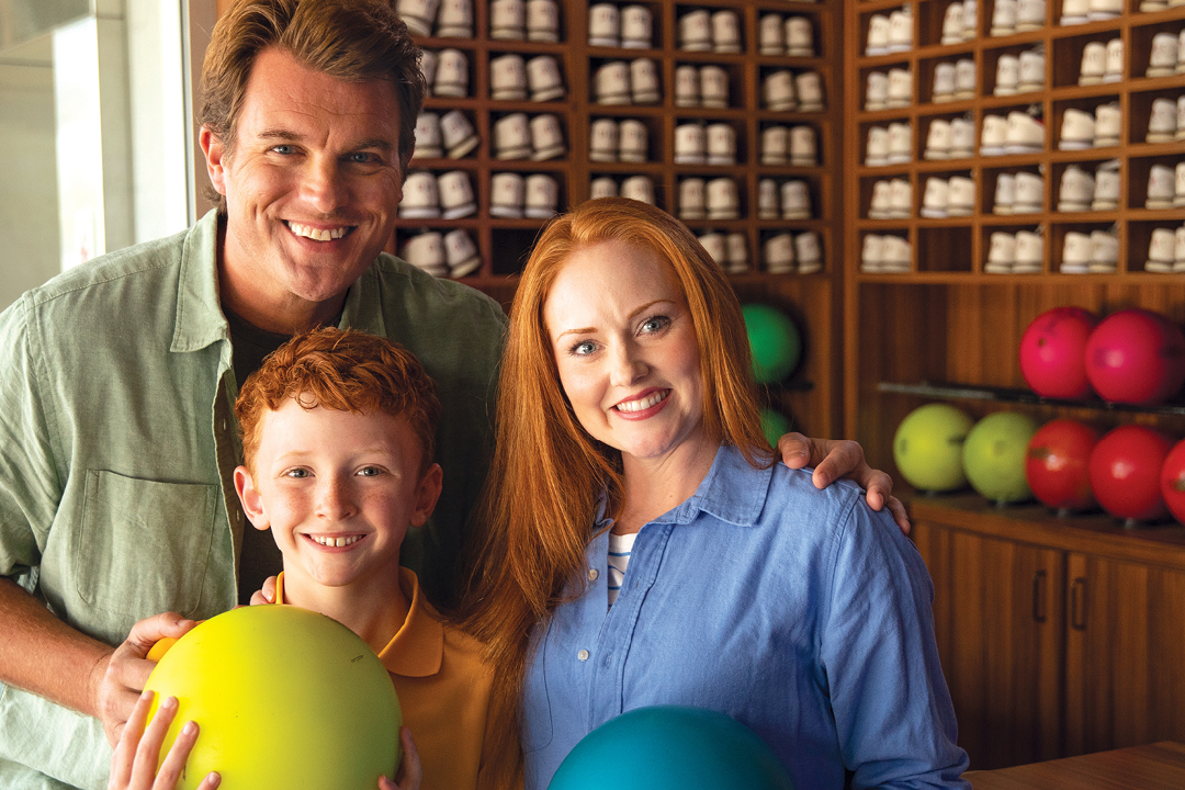 A dad, mom and son standing together while holding bowling balls