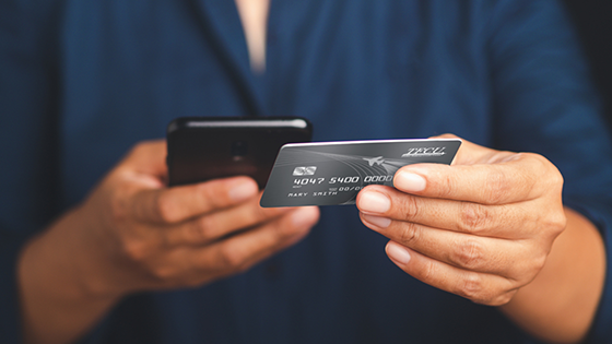 Close up of someone holding a TFCU Visa credit card and mobile device.