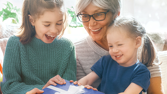 A grandma with her two grandkids holding a present.