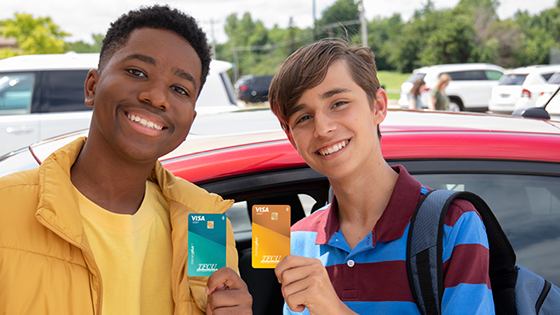 Two teen boys standing in front of the a red car while both are hold up Moneyplus cards.