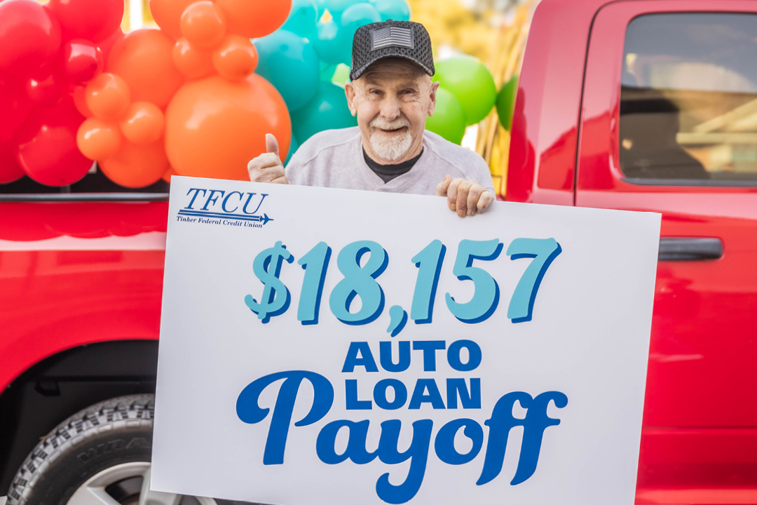 An older man who is a TFCU member is holding a sign in front of a red truck that says $18,157 auto loan payoff