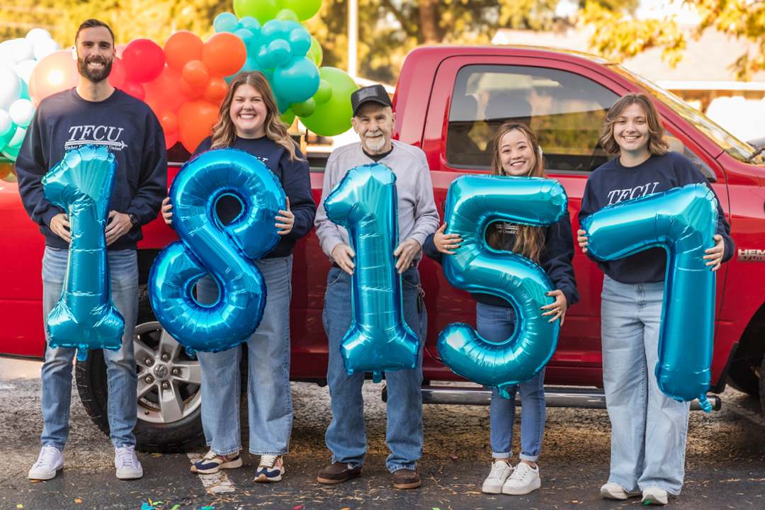 A group of 5 people standing in front of a red truck while holding number balloons