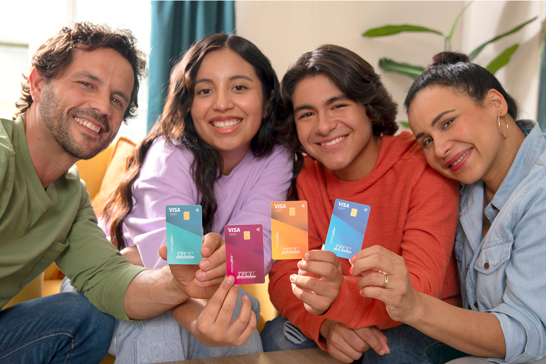 A family of four looking at the camera and smiling while holding up MoneyPlus cards