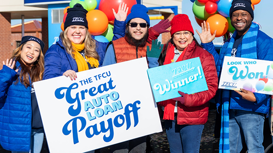 A mom and son with TFCU employees standing in front of balloons holding a sign that says auto loan payoff.