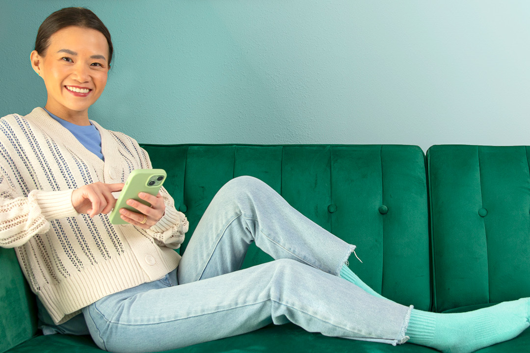 A young woman sitting across a green sofa while on her mobile device.