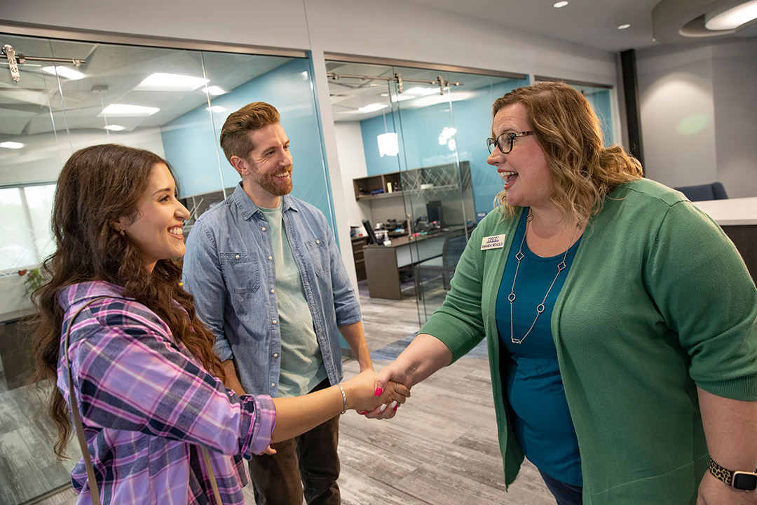 A TFCU employee shaking hands with a young woman with a young man next to her.