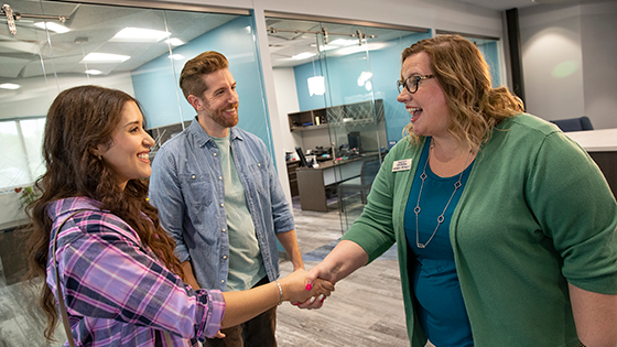 A TFCU employee shaking hands with a young woman with a young man next to her.