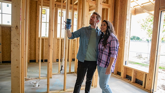 A young couple standing in a construction home and looking at something in the distance.