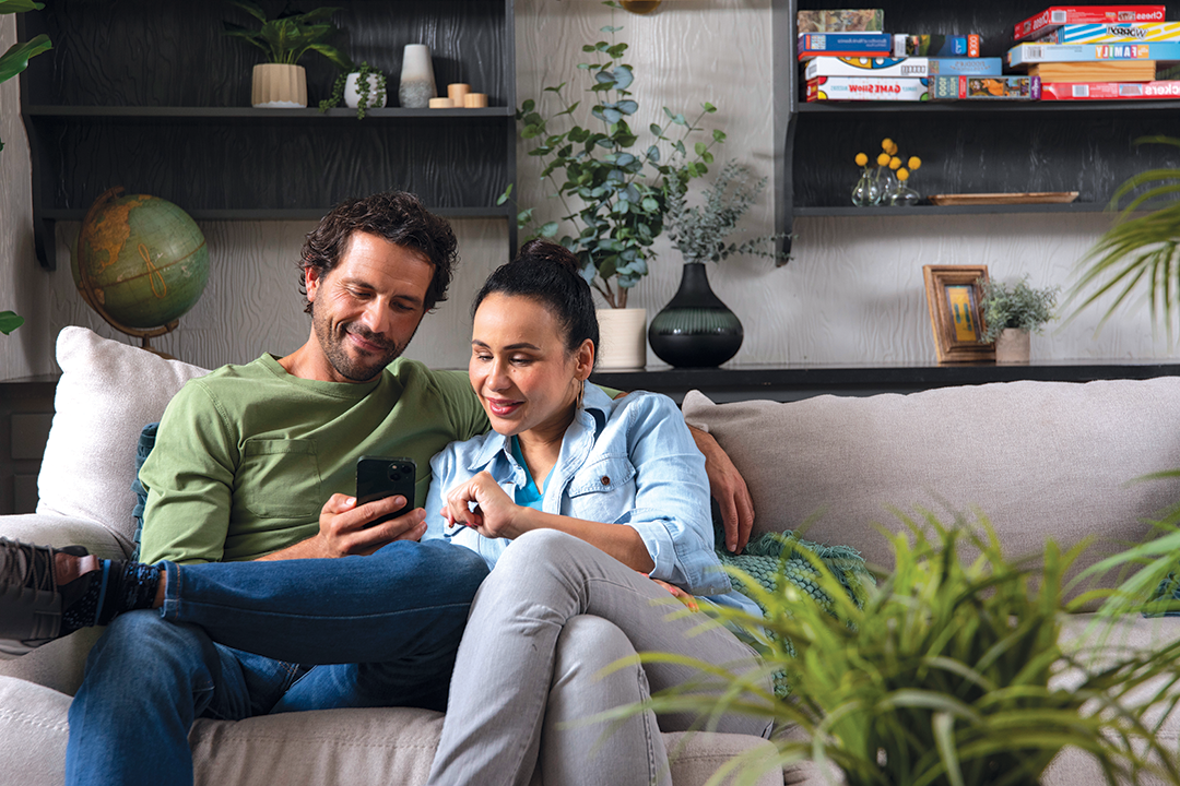 Mom and dad sitting together on a couch while looking at a mobile device