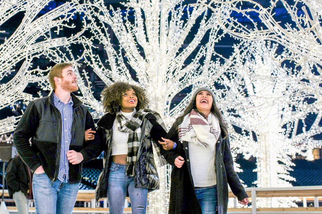 A group of three friends looking at tree lights.