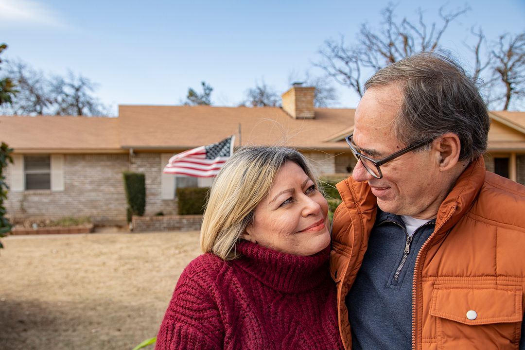 Two older couple looking at each other with their house in the background