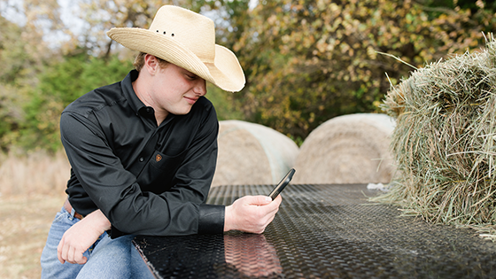 Young cowboy leaning on his truck while on his smartphone