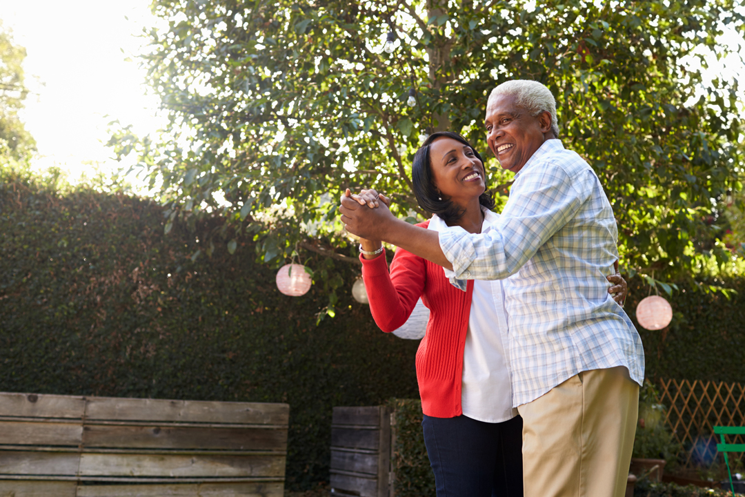 older couple holding each other close and dancing and smiling outdoors